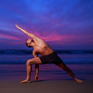 Man in stretching yoga pose on ocean beach at dusk