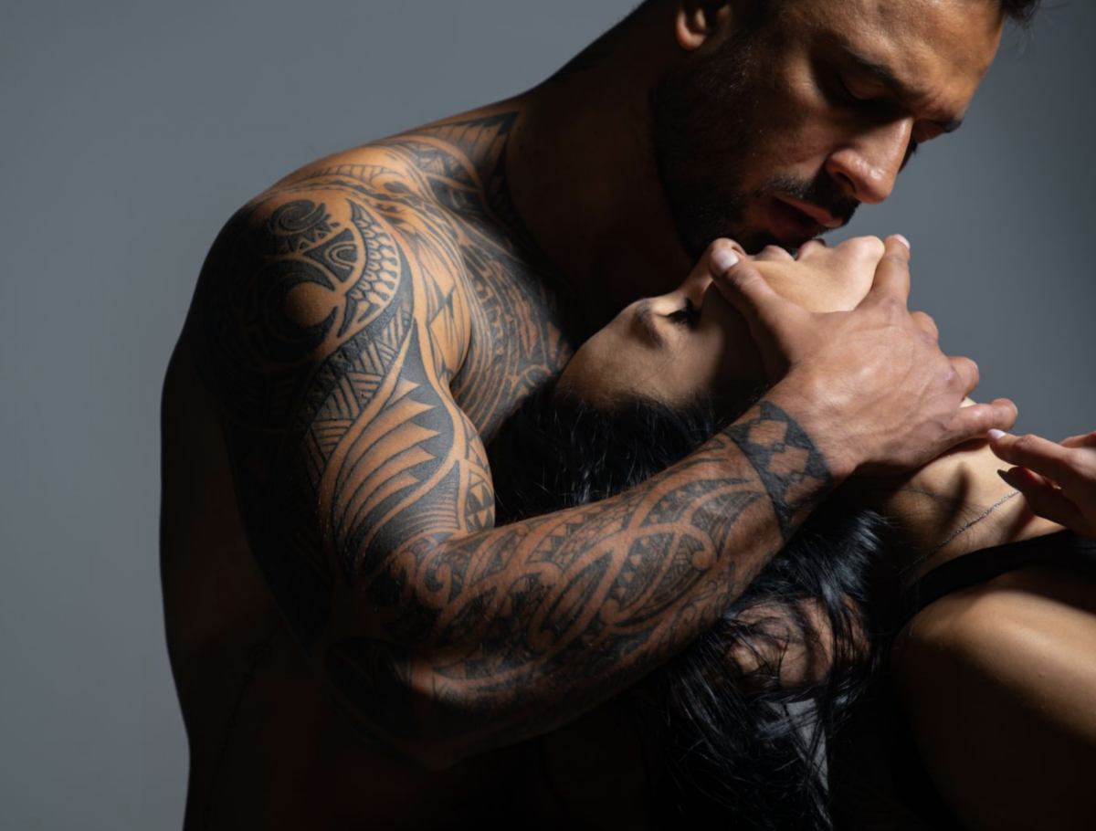 tattooed man holding his woman from behind with her neck and head tilted up and back